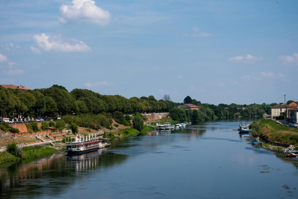 Tranquil view of the river and boats in Pavia, Italy under a blue sky.
